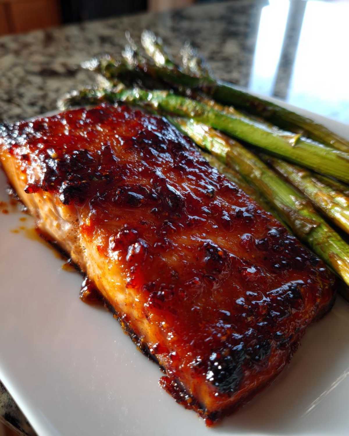 Close-up of a perfectly cooked salmon fillet with a thick, glossy Gochujang Honey Glazed Salmon coating, served next to roasted asparagus.