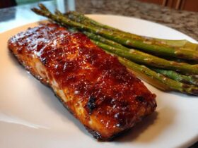 Close-up of a glistening Gochujang Honey Glazed Salmon fillet served with roasted asparagus on a white plate.