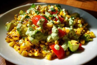 Close-up of a delicious grilled Corn Salad featuring charred corn kernels, avocado chunks, red tomatoes, and a creamy green dressing.
