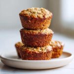 A stack of three golden brown Healthy Banana Oatmeal Muffins topped with visible oats, resting on a small plate.