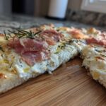 Close-up of a slice of Honey Ricotta Pizza topped with creamy ricotta, prosciutto, and fresh rosemary sprigs.