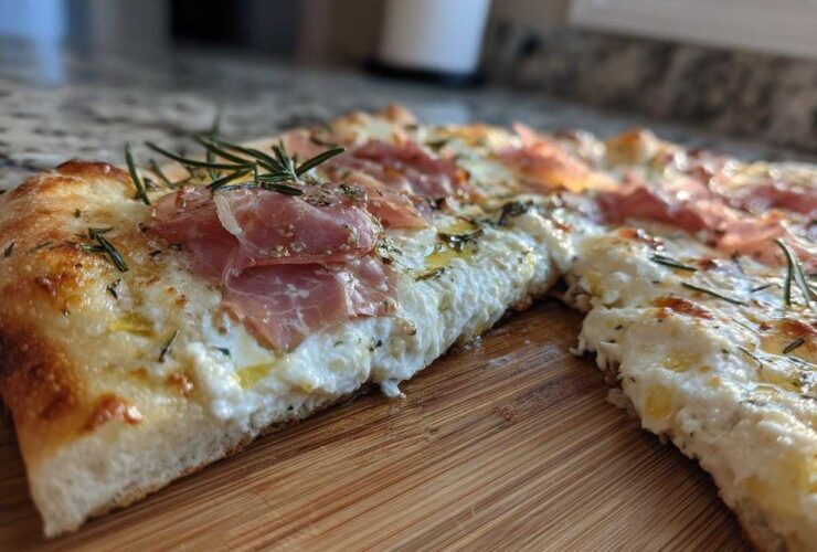 Close-up of a slice of Honey Ricotta Pizza topped with creamy ricotta, prosciutto, and fresh rosemary sprigs.
