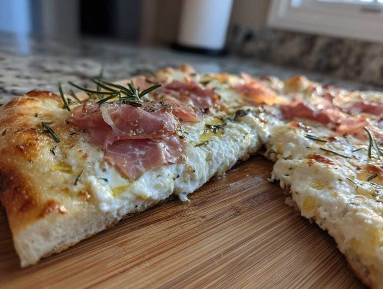 Close-up of a slice of Honey Ricotta Pizza topped with creamy ricotta, prosciutto, and fresh rosemary sprigs.