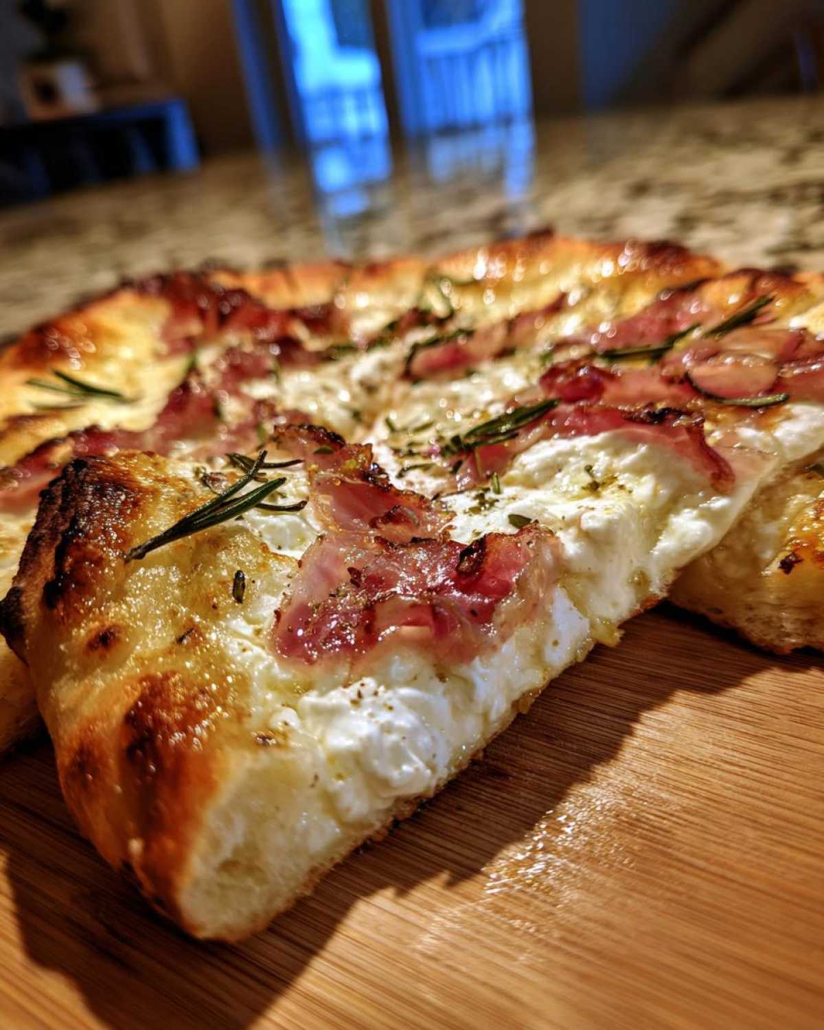 Close-up of a thick-crust Honey Ricotta Pizza slice topped with creamy ricotta, prosciutto, and fresh rosemary.