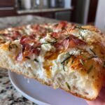 A thick slice of Honey Ricotta Pizza featuring fluffy crust, dollops of white ricotta cheese, crispy prosciutto, and a drizzle of honey.
