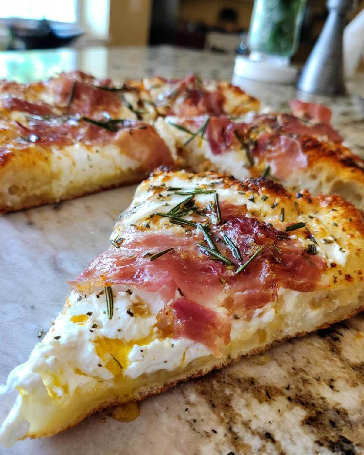 Close-up of a thick slice of Honey Ricotta Pizza topped with creamy ricotta, prosciutto, and fresh rosemary.