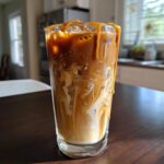 A tall glass of Iced Caramel Swirl Coffee showing beautiful swirls of cream and coffee, topped with caramel drizzle.