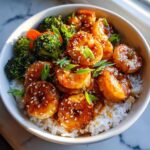 Close-up of Irresistible Honey Garlic Shrimp Bowls served over white rice with steamed broccoli and carrots, topped with sesame seeds.