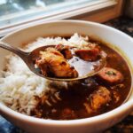 A spoonful of rich Justin Wilson Chicken and Sausage Gumbo over white rice in a white bowl.