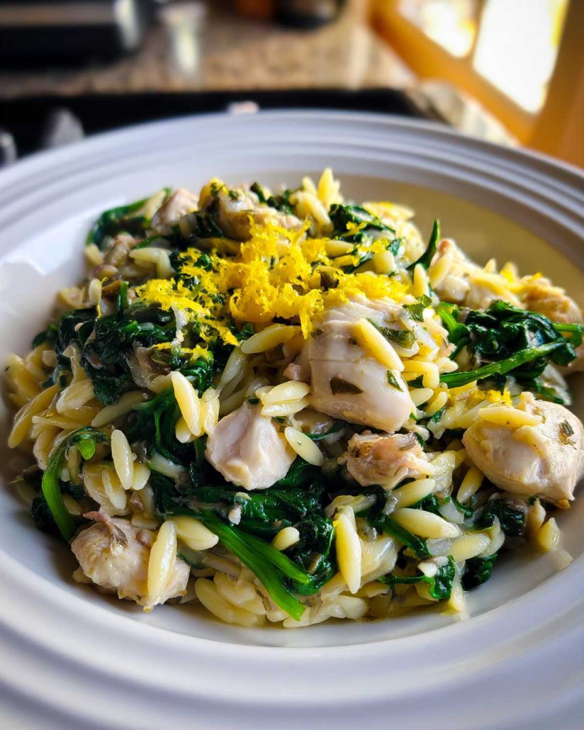 A close-up serving of Lemon Chicken Orzo Spinach topped with bright yellow lemon zest in a white bowl.