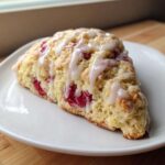 A single, triangular Lemon Raspberry Scone topped with white lemon glaze, served on a white plate.