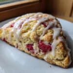 A single wedge of Lemon Raspberry Scones, topped with a thick white glaze, resting on a white plate.