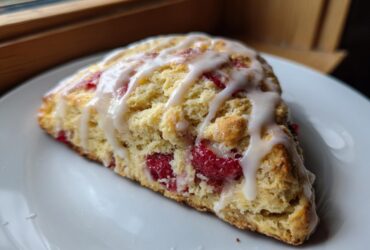 A single wedge of Lemon Raspberry Scones, topped with a thick white glaze, resting on a white plate.