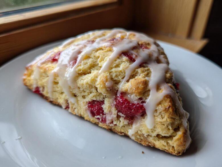 A single wedge of Lemon Raspberry Scones, topped with a thick white glaze, resting on a white plate.
