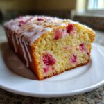 A freshly baked loaf of Lemon Rhubarb Bread with a white glaze drizzled over the top, resting on a white plate.