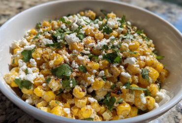 A close-up view of Mexican Street Corn Salad Esquites featuring charred corn kernels, cotija cheese, cilantro, and chili powder in a white bowl.