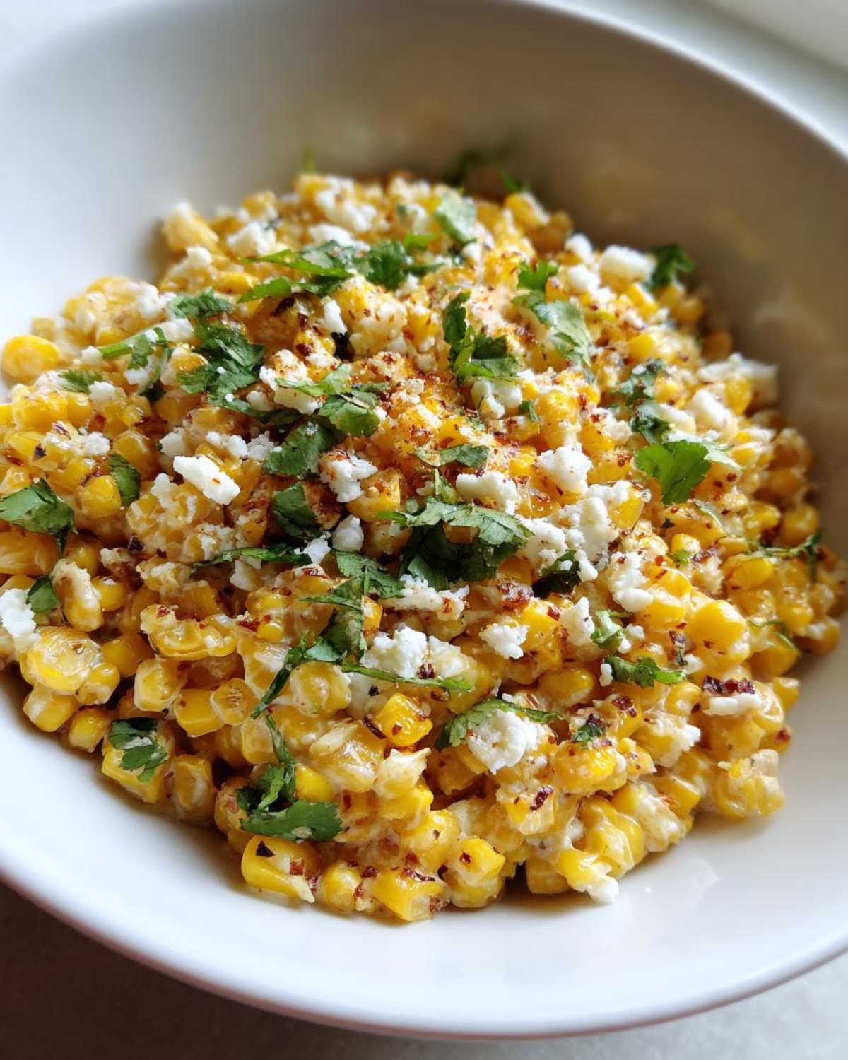 A close-up view of Mexican Street Corn Salad Esquites, featuring creamy corn kernels topped with cotija cheese, cilantro, and chili powder.