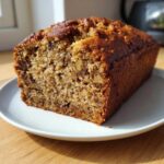 A close-up of a freshly baked loaf, showing the crumb structure of the Moist Banana Bread studded with walnuts.