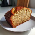 A close-up, sunlit slice of moist Banana Bread showing its golden-brown crust and tender crumb.