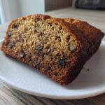 A thick slice of incredibly moist banana bread showing a rich crumb texture and visible walnuts.