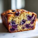 Close-up of a moist slice of Blueberry Banana Bread showing rich yellow crumb studded with juicy blueberries.