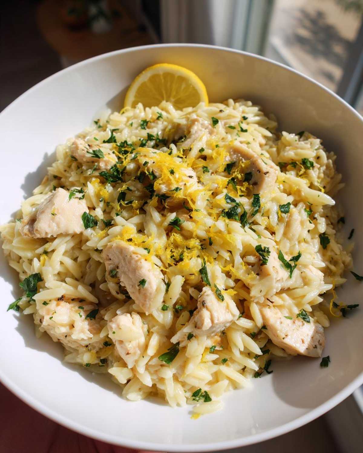 Close-up of creamy Chicken Orzo mixed with diced chicken, topped with fresh parsley and lemon zest.