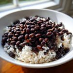 Close-up of a white bowl filled with fluffy white rice topped generously with savory, seasoned black beans and rice.