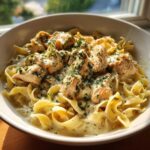 A close-up of a white bowl filled with creamy One Pot Chicken and Noodles, topped with fresh parsley.