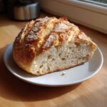 A half loaf of crusty Quick and French Bread with an open crumb structure resting on a small white plate.