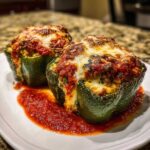 Two baked green Ricotta Stuffed Peppers topped with marinara sauce and melted, browned mozzarella cheese.