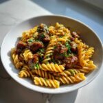 Close-up of Simple Sticky Honey Garlic Sausage Pasta Skillet Recipe served in a white bowl, garnished with parsley.
