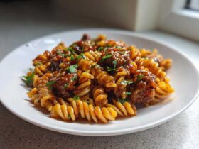 A close-up of fusilli pasta mixed with sausage pieces coated in a sticky honey garlic sauce, garnished with parsley.