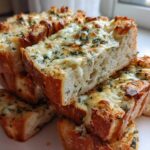A stack of freshly baked Sliced Garlic Bread with Cheese, featuring melted cheese and green herbs on golden crusts.