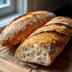 Two loaves of freshly baked Sourdough French Bread cooling, one sliced to show the open, airy crumb structure.