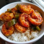 Close-up of a white bowl filled with white rice topped with vibrant, seasoned Spicy Cajun Shrimp and green bell peppers.