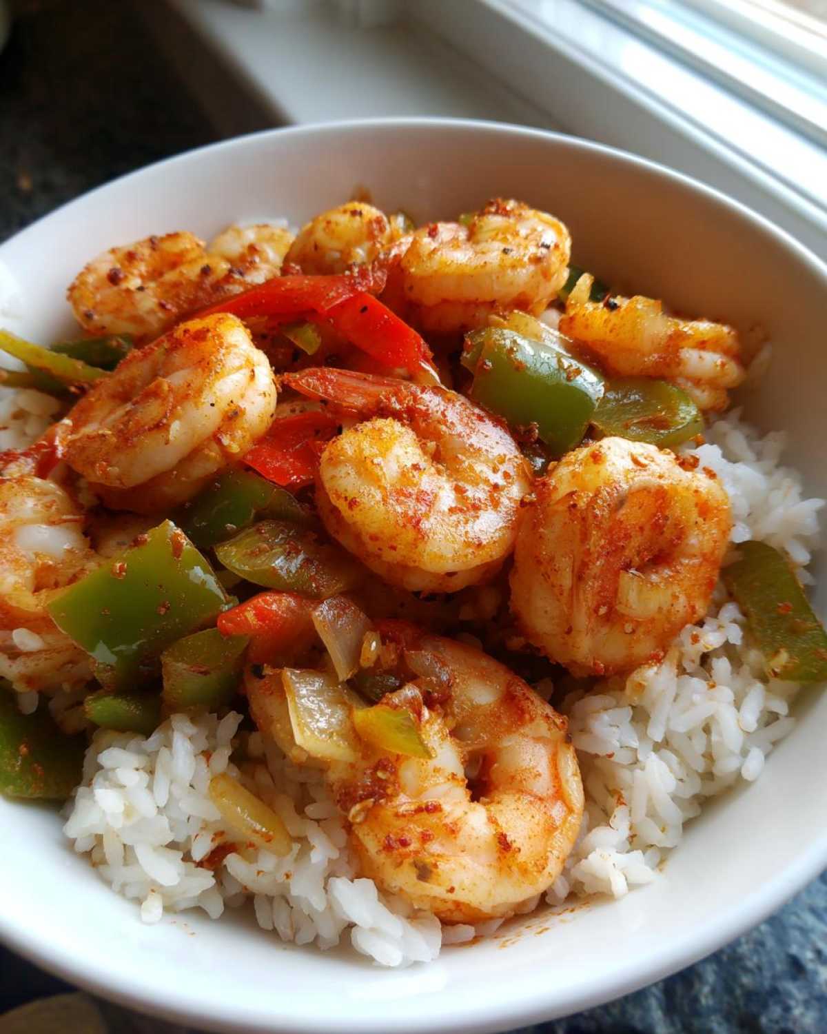 Close-up of a Spicy Cajun Shrimp & Rice Bowl featuring seasoned shrimp, red and green peppers over white rice.