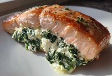 A close-up of a golden-brown, baked Spinach Stuffed Salmon fillet oozing creamy spinach filling on a white plate.