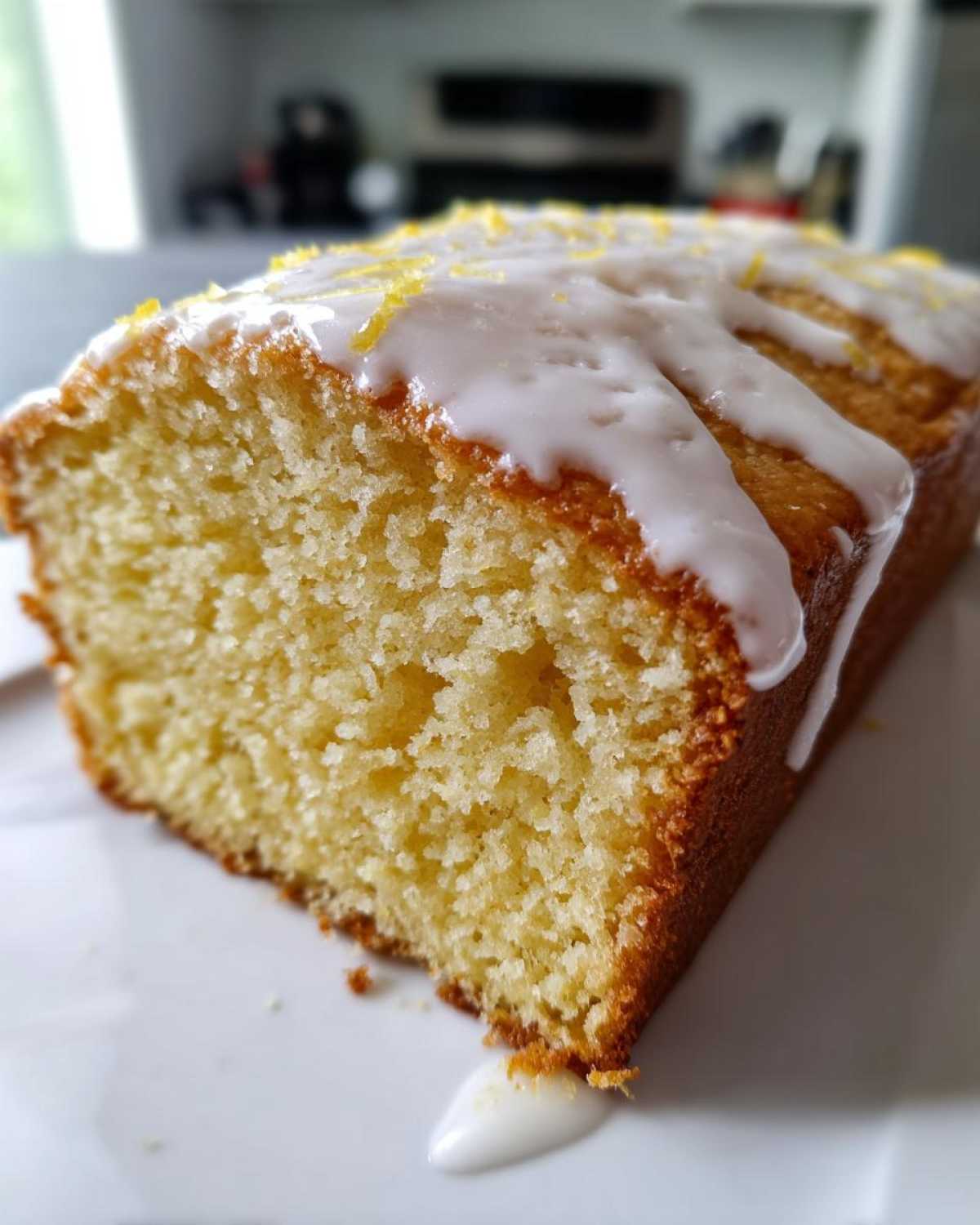Close-up of a moist slice of Starbucks Lemon Loaf, drizzled with white icing and topped with lemon zest.