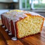 A close-up of a freshly baked Starbucks Lemon Loaf, sliced to show the moist crumb and topped with thick white lemon glaze.