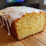 A close-up view of a freshly baked Starbucks Lemon Loaf, featuring a thick, dripping white glaze and lemon zest.