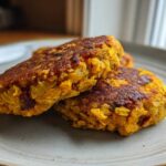 Close-up of two golden-brown Sweet Potato Lentil Patties stacked slightly on a light gray plate.