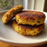 Close-up of three golden-brown Sweet Potato Lentil Patties stacked on a speckled plate, one patty cut open.