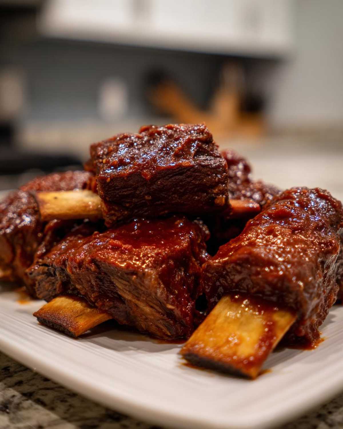 Close-up of tender Crock Pot Short Ribs piled on a white plate, heavily coated in a rich, dark barbecue glaze.