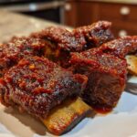Close-up of four tender Crock Pot Short Ribs coated in a thick, glossy, dark red barbecue-style sauce.