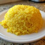 A perfectly molded mound of bright yellow Texas Roadhouse Seasoned Rice served on a white plate.