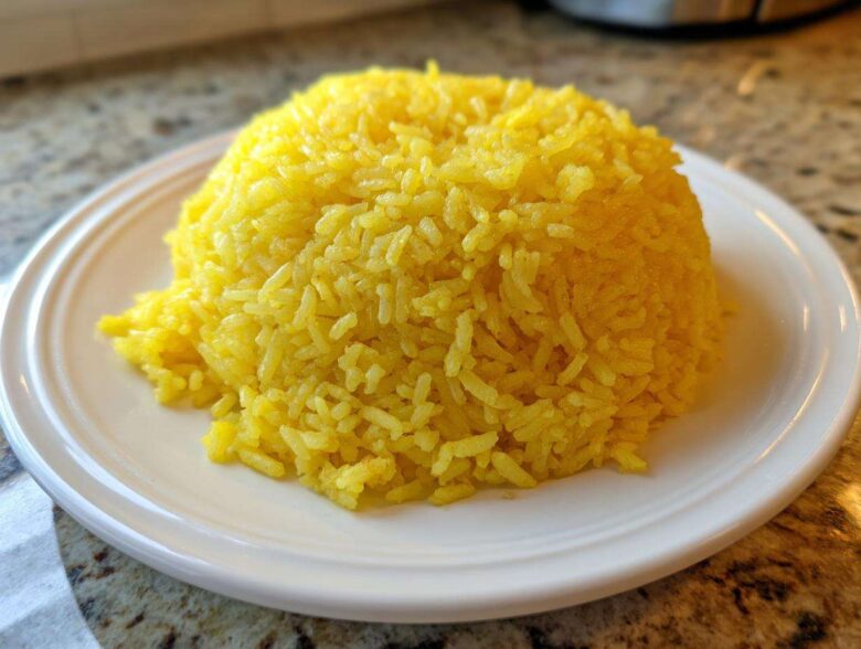 A perfectly molded mound of bright yellow Texas Roadhouse Seasoned Rice served on a white plate.